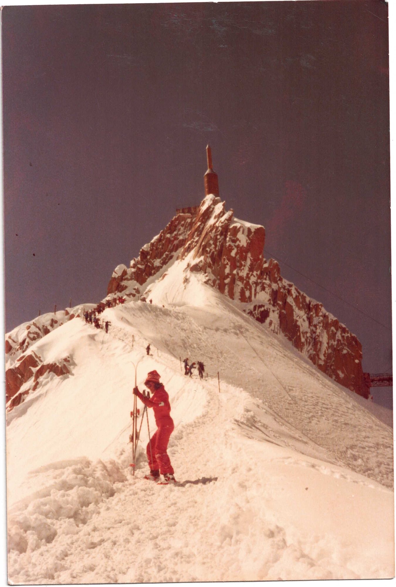 Klättrare i rött på snökammen vid Aiguille du Midi, toppstationen ovanför